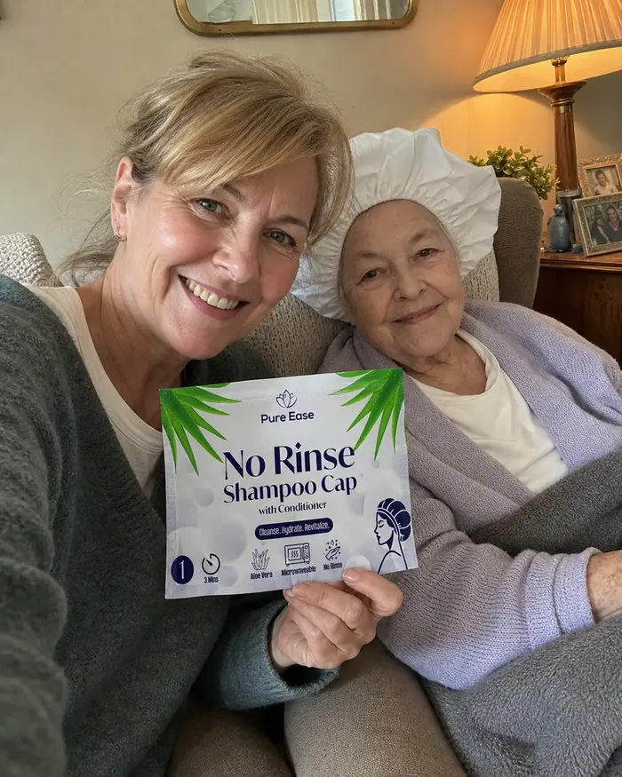 Smiling daughter and elderly mother on the sofa, mum wearing a PureEase no-rinse shampoo cap and holding the sachet